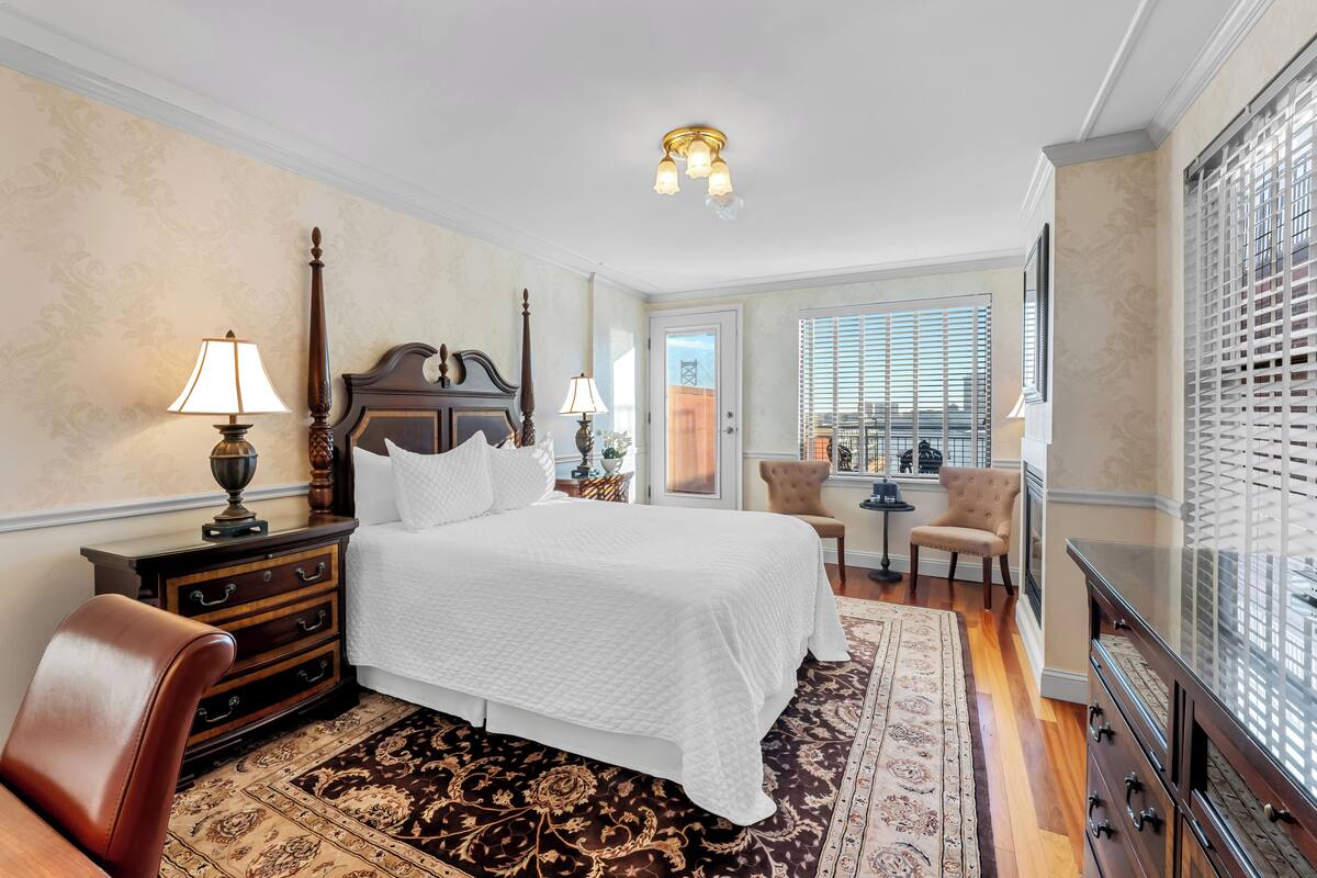 A hotel room with a bed, a desk, a chair, a dresser, a lamp, and a window with blinds.