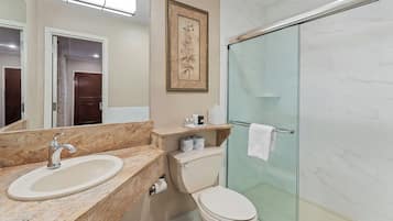 A bathroom with a marble sink, toilet, and glass shower enclosure.
