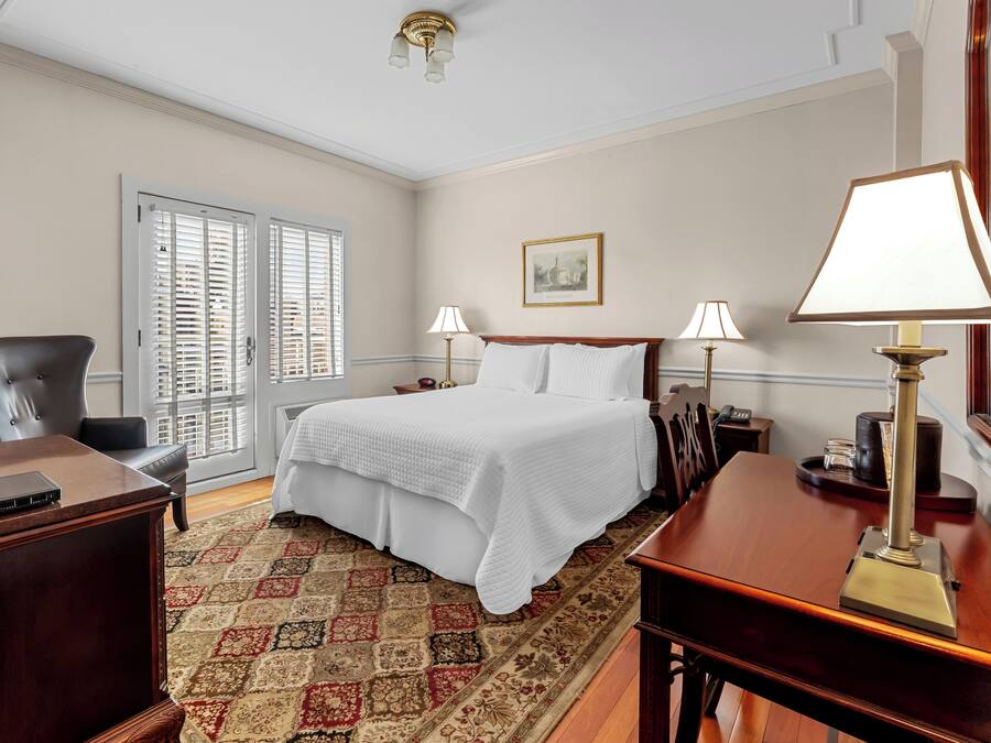 A hotel room with a large bed, two bedside lamps, a desk with a lamp, a chair, a television, and a patterned rug.