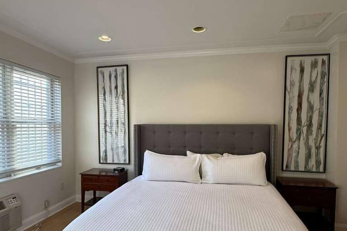 A large bed with a grey headboard, two bedside tables, and artwork on the walls.
