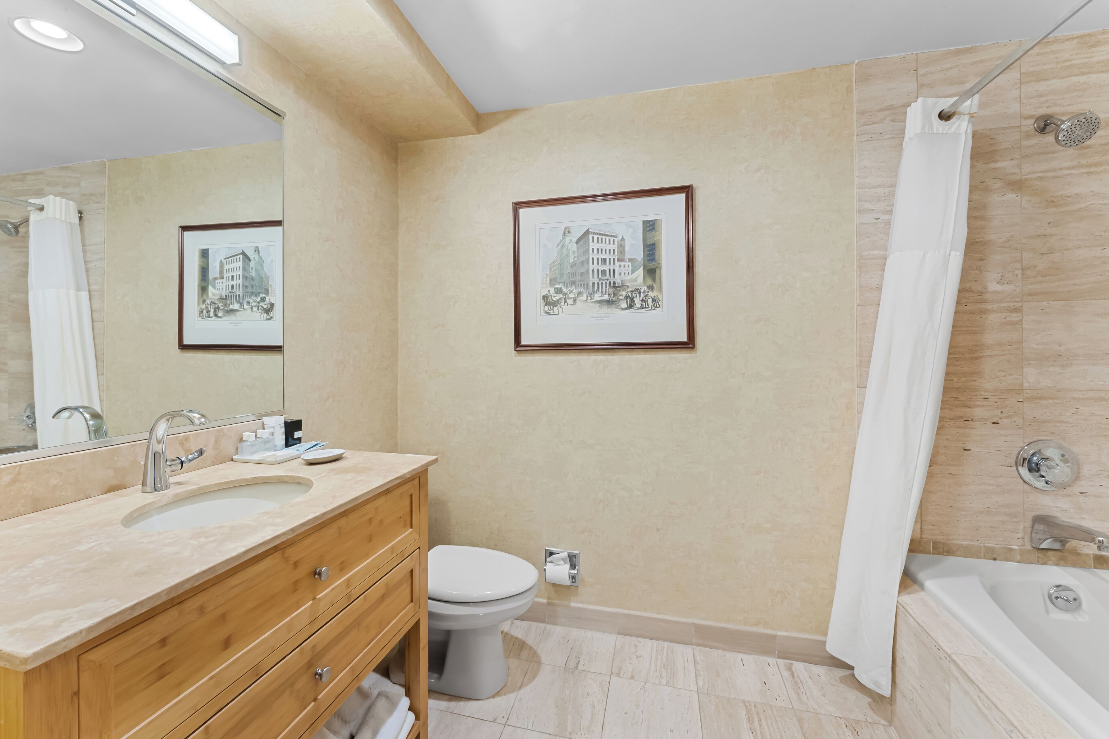A modern bathroom with a sink, toilet, and bathtub. There are framed pictures on the wall and a shower curtain.