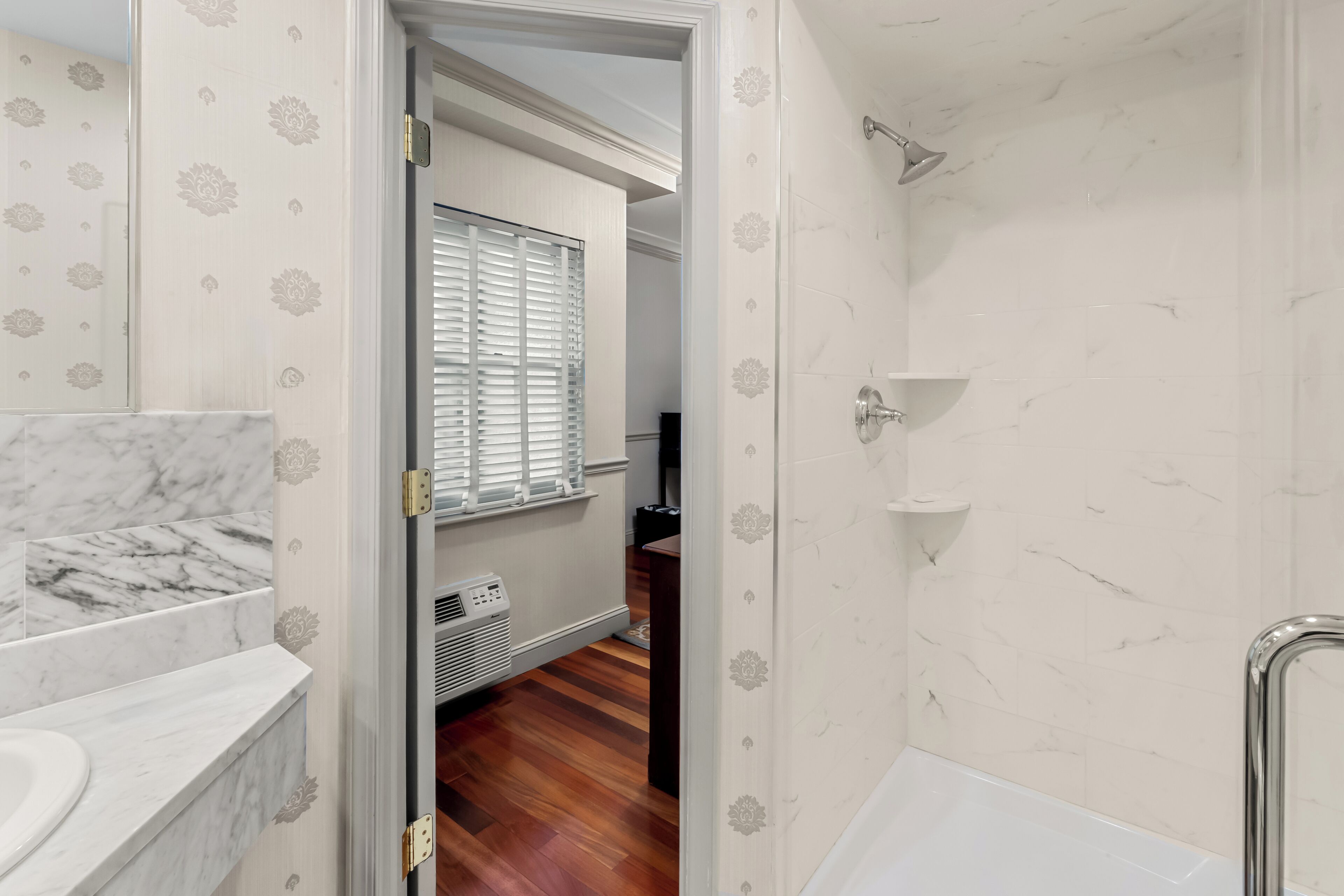 A bathroom with a white marble sink, a shower with a handheld showerhead, and a wooden floor.
