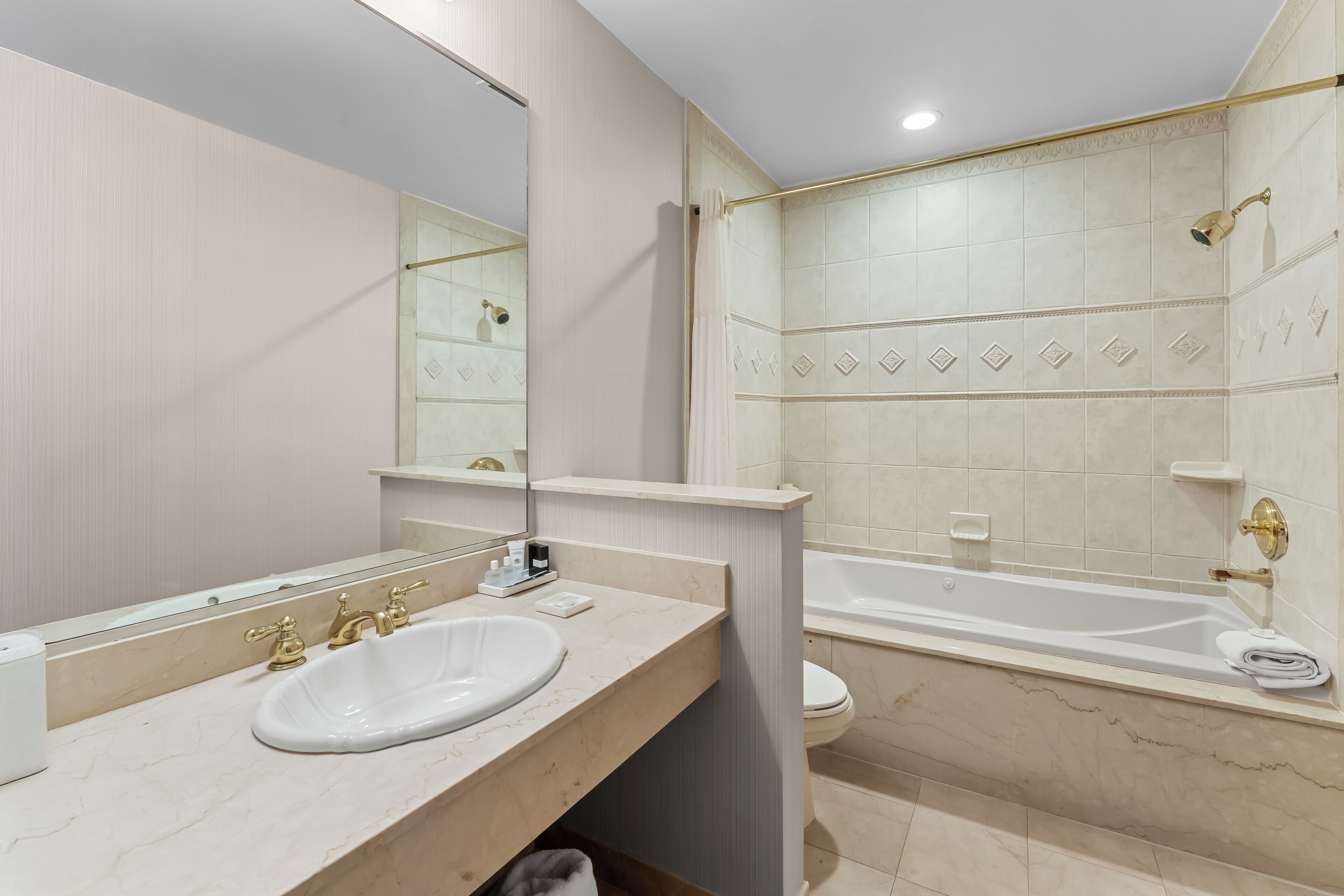 Un baño moderno con un lavamanos blanco, grifos dorados, un espejo grande y una bañera.