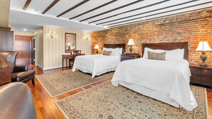 Habitación de hotel con dos camas, pared de ladrillo, vigas de madera en el techo y una alfombra grande.