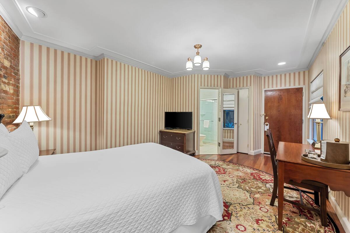 A hotel room with a large bed, a desk, a television, and a bathroom visible through an open door.