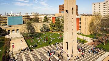A plaza with a central monument, surrounding buildings, and a grassy area with people.