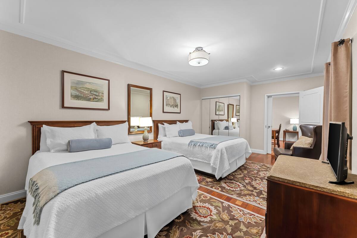 A hotel room with two beds, a television, a desk, and a mirror.