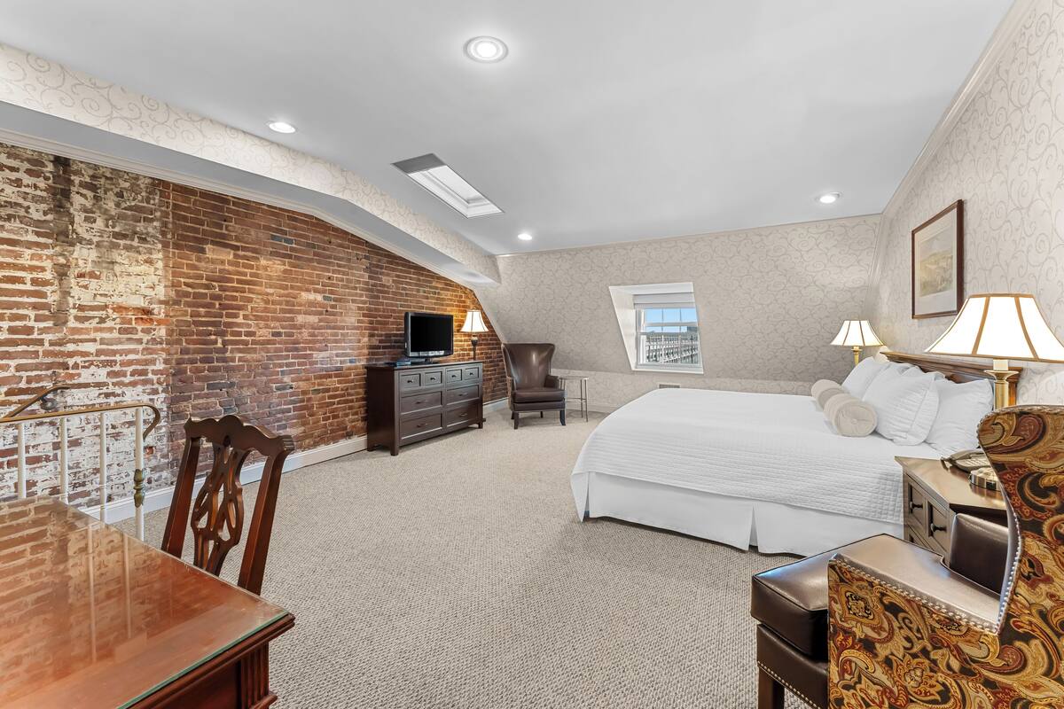 A hotel room with a brick wall, a bed, a desk, and a chair.
