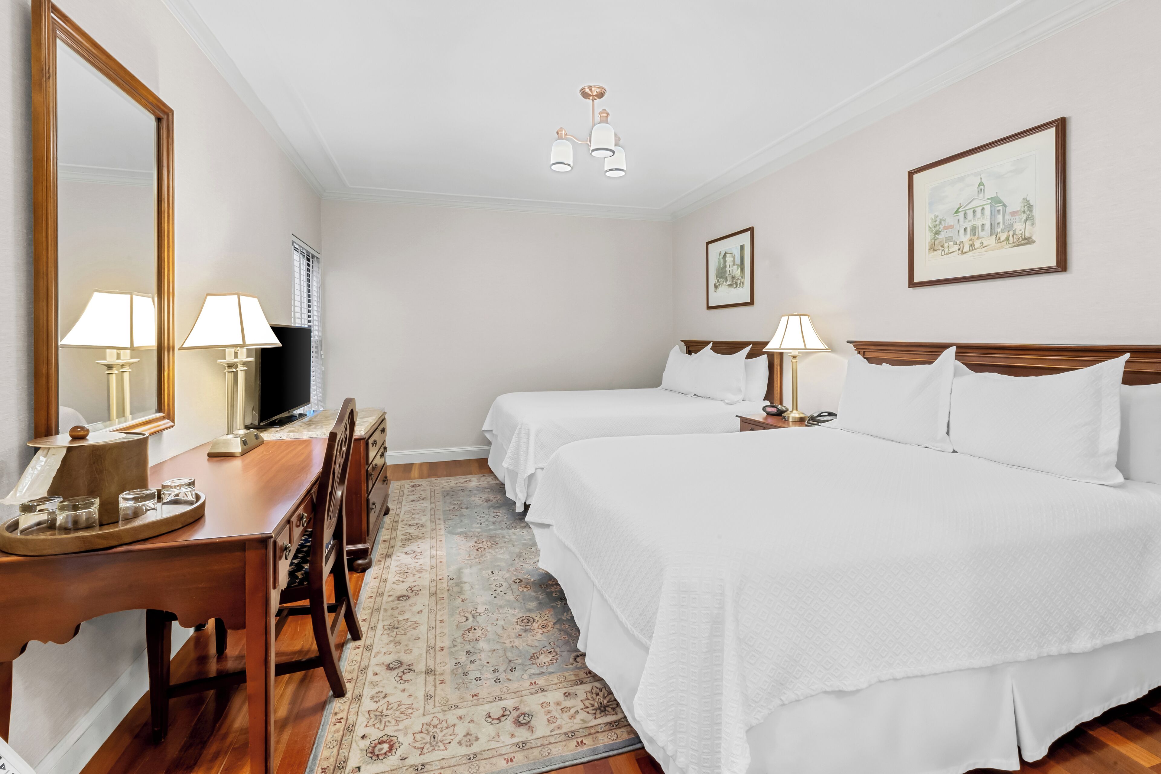 Una habitació d'hotel amb dos llits, un escriptori amb làmpades, televisió i un mirall gran.