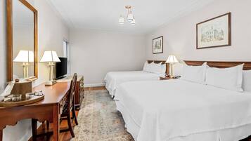 A hotel room with two beds, a desk with lamps, a television, and a large mirror.