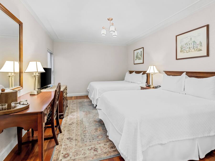 A hotel room with two beds, a desk with lamps, a television, and a large mirror.