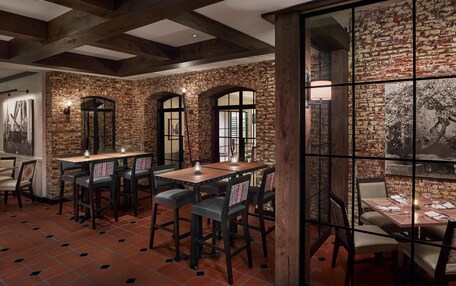 A restaurant with brick walls, wooden beams, and tiled floors. Tables and chairs are arranged for dining.