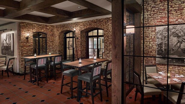Un restaurante con paredes de ladrillo, vigas de madera y suelos de baldosas. Mesas y sillas dispuestas para comer.