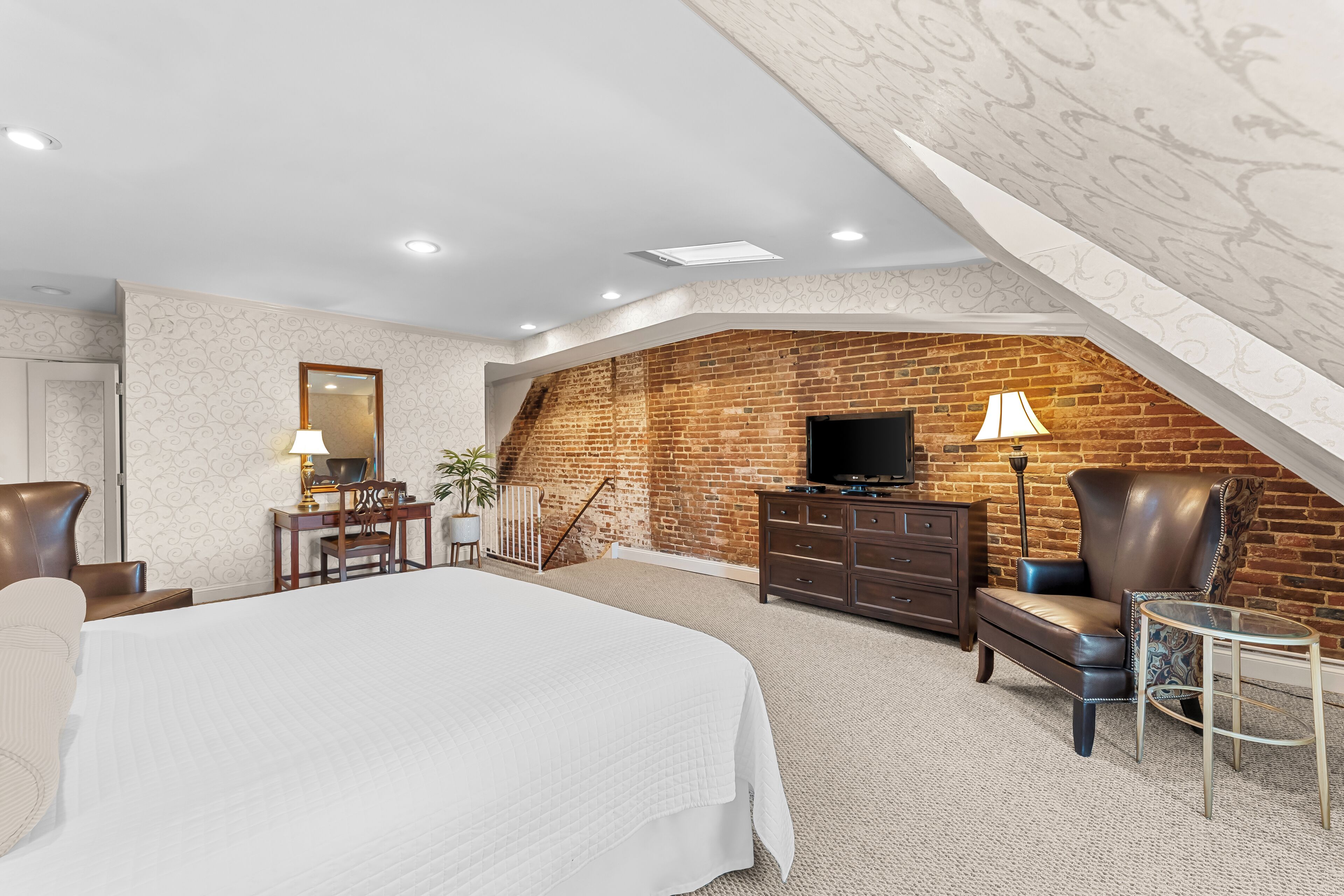 A bedroom with a large bed, a TV, a desk with a lamp, and a chair.