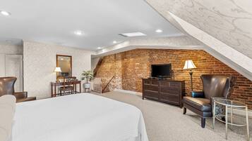 A bedroom with a large bed, a TV, a desk with a lamp, and a chair.