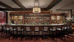 Una zona de bar con una barra alargada, varios estantes llenos de botellas y varios taburetes.
