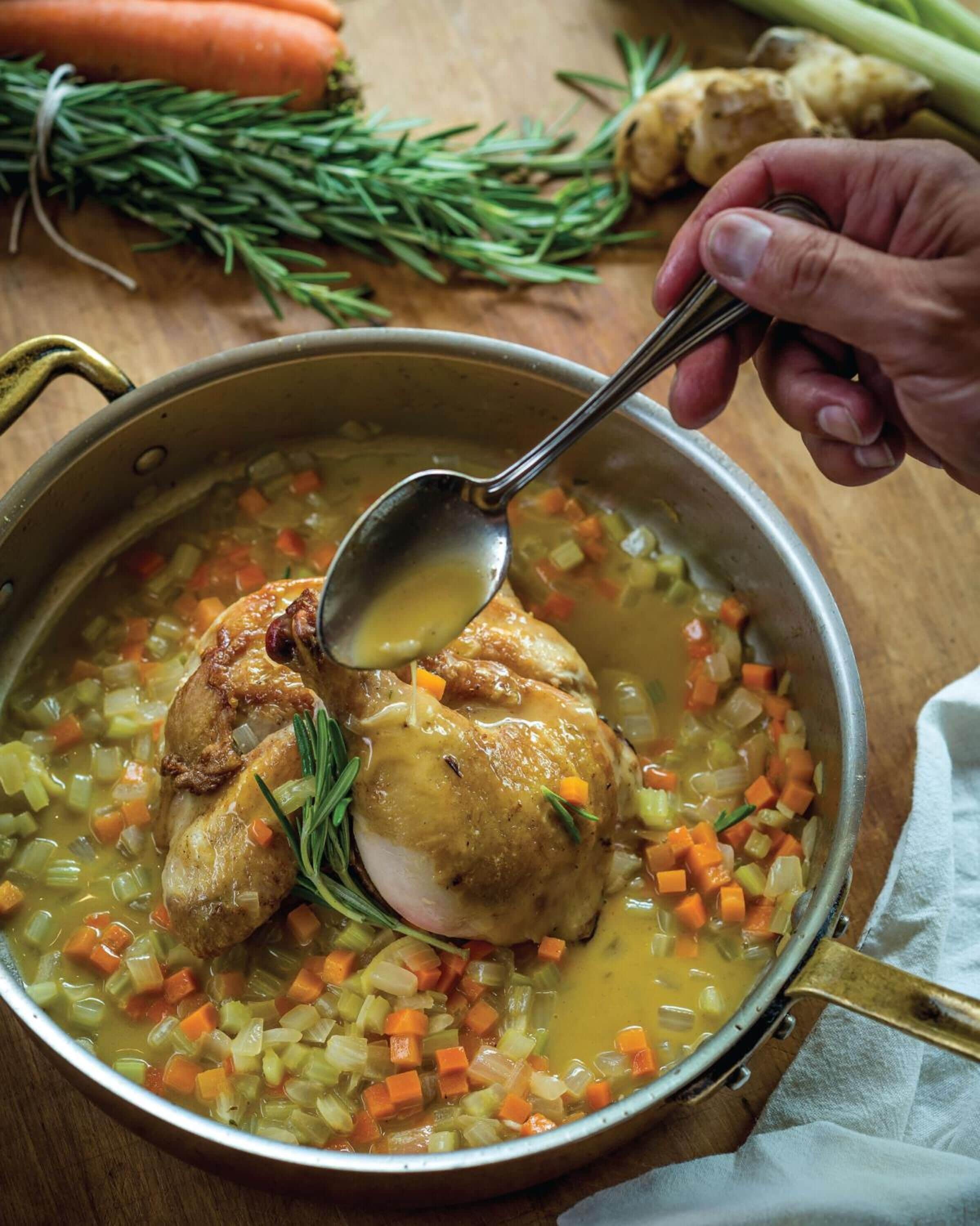 A pot of soup with a roasted chicken and vegetables.