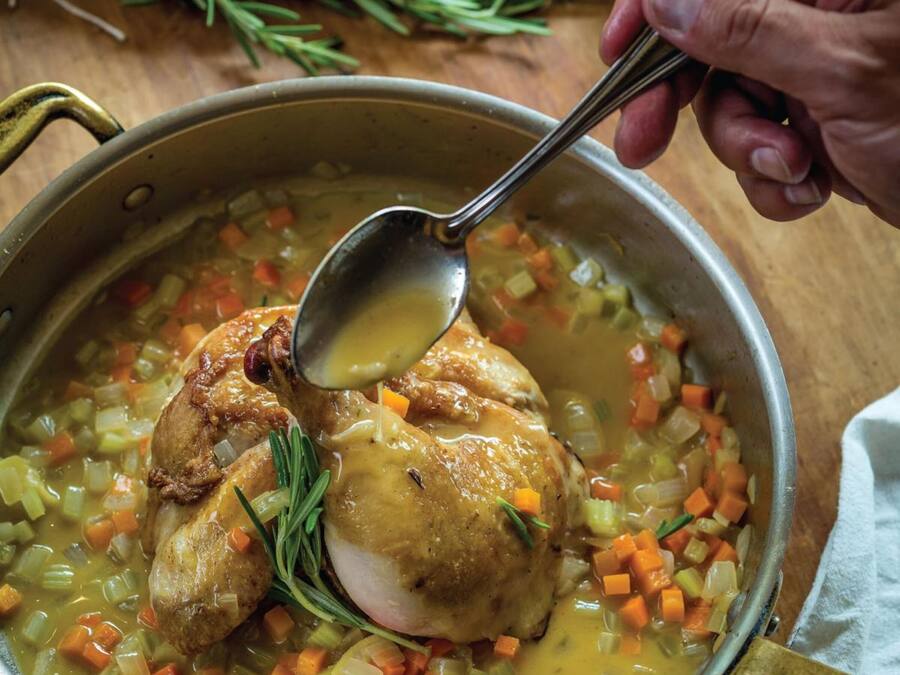 A pot of soup with a roasted chicken and vegetables.