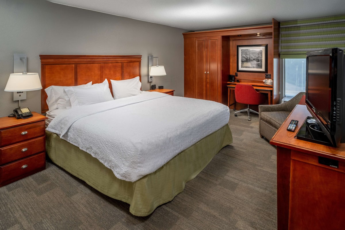 A hotel room with a large bed, a desk with a chair, a television, and a wardrobe.