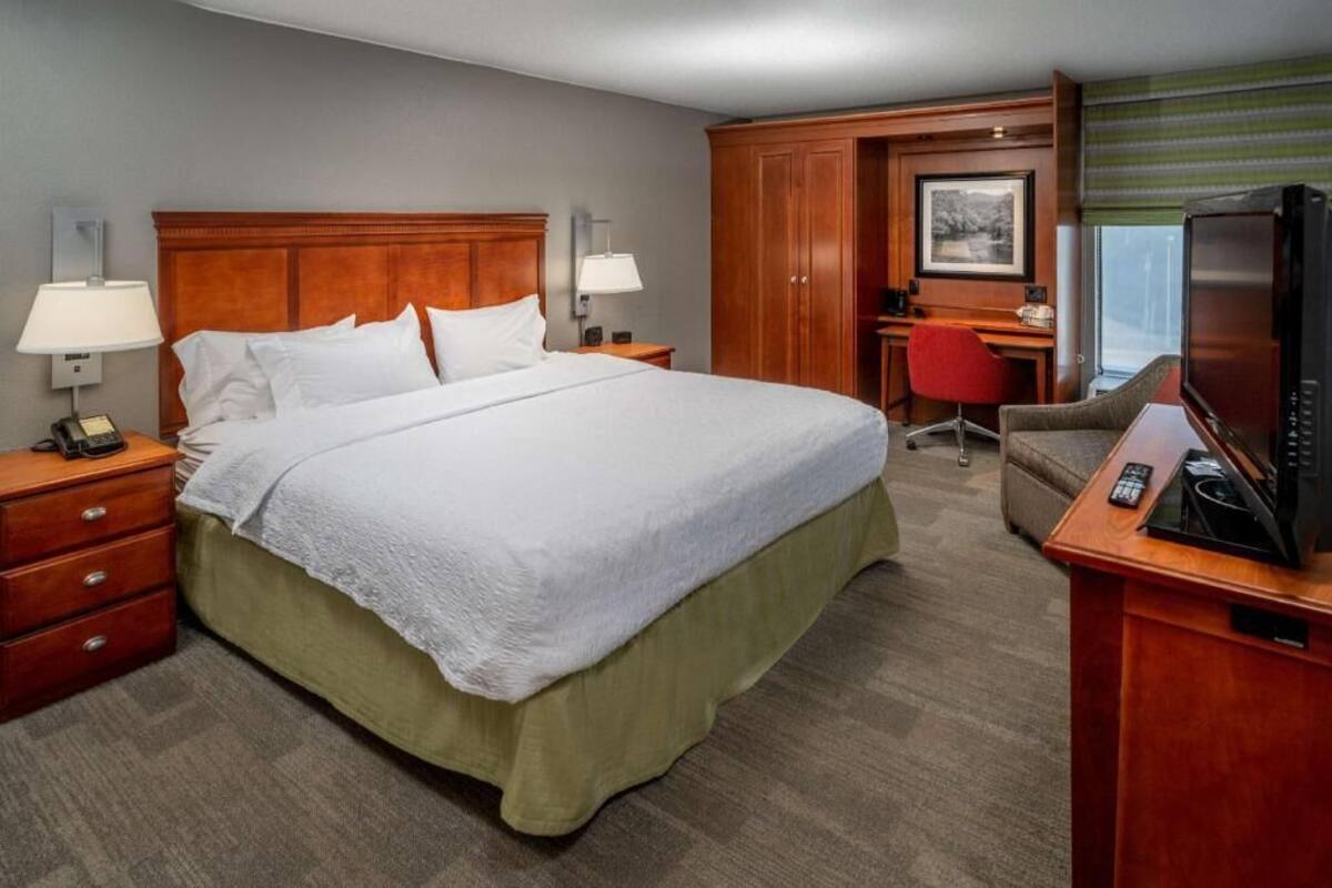 Quarto de hotel com cama, escrivaninha, cadeira, televisão e telefone.