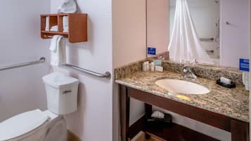 A bathroom with a white toilet, a wooden shelf with towels, a granite sink, and a mirror with a light fixture.