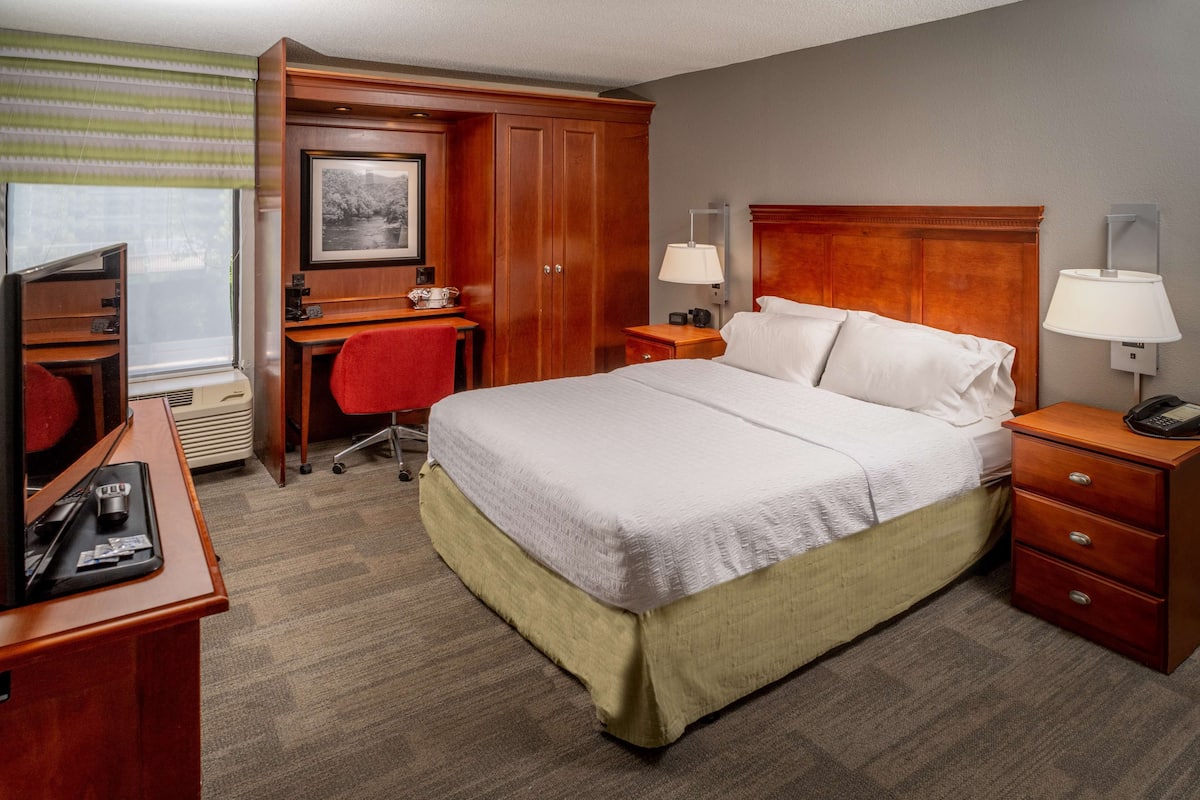 A hotel room with a bed, desk, chair, and a television.