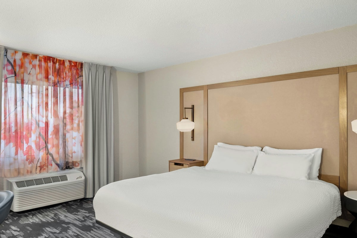 A hotel room with a large bed, a bedside table with a lamp, and a window with curtains.