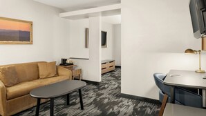 A modern hotel room with a sofa, a small table, a TV mounted on the wall, and a desk with a lamp. - Fairfield by Marriott Mt Pleasant (Mount Pleasant)