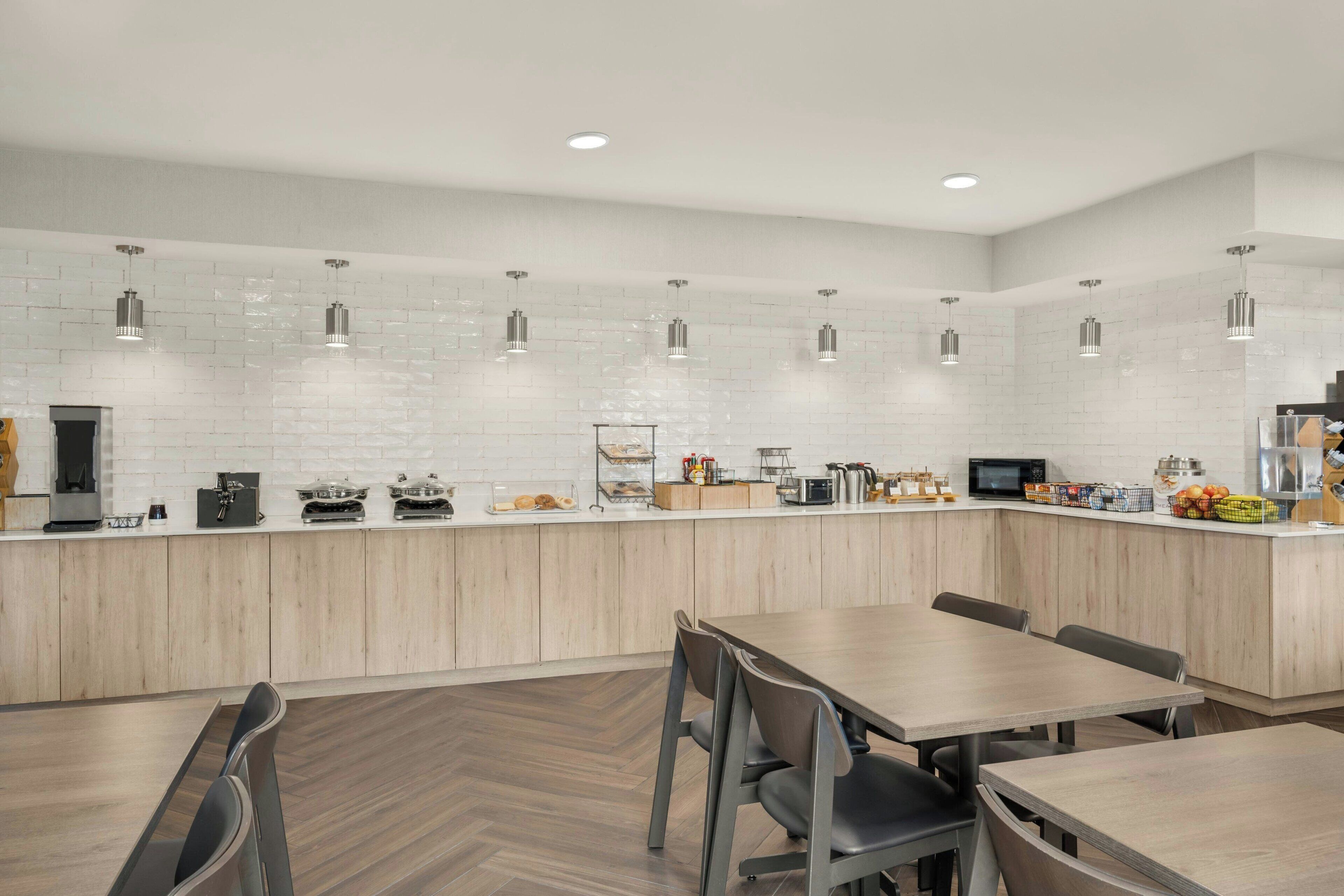 A modern kitchen with white brick backsplash, wooden cabinets, and pendant lighting.
