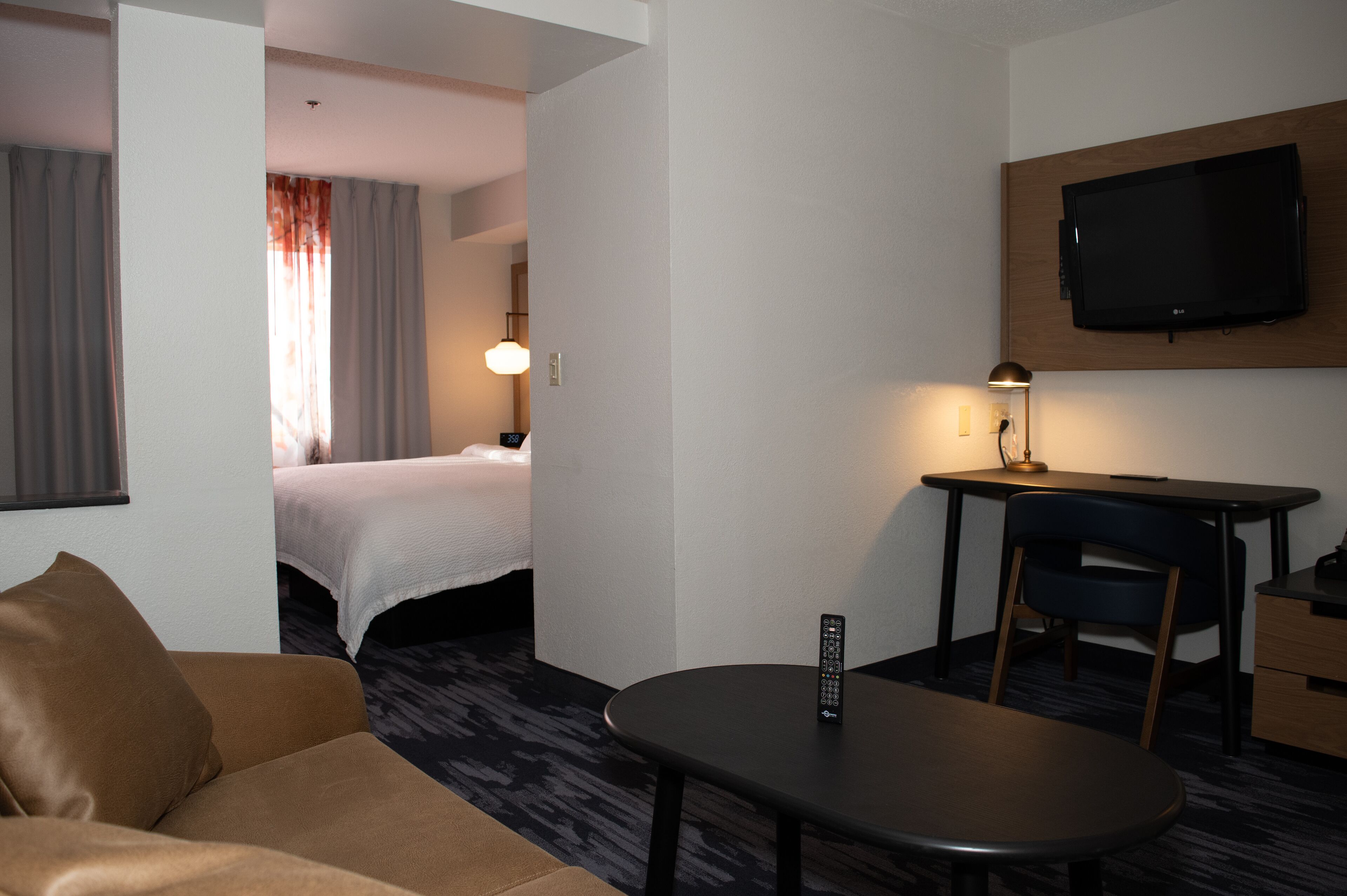 Habitación de hotel con una cama, un escritorio con una lámpara, un televisor montado en la pared y un control remoto sobre el escritorio.