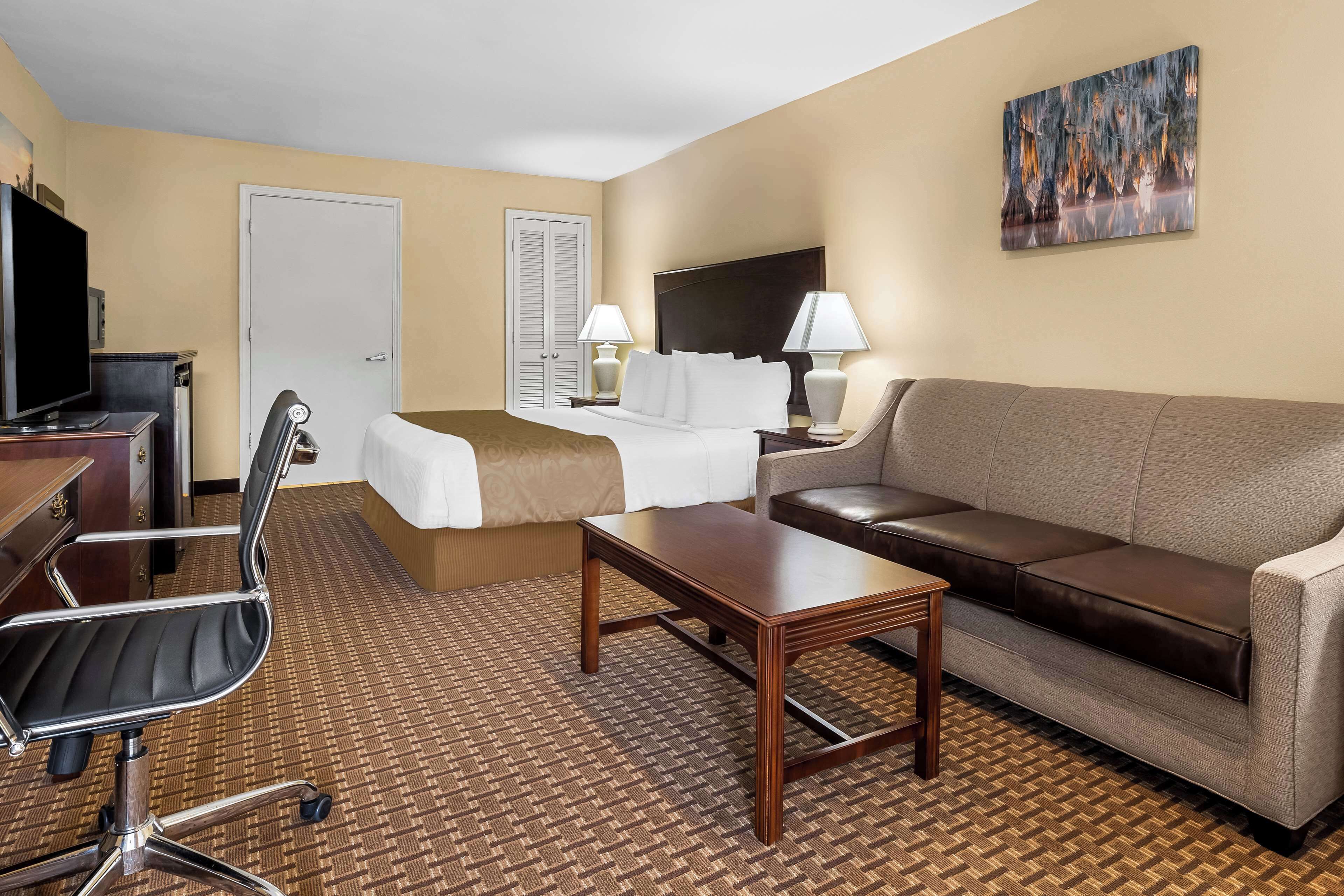 A hotel room with a bed, a sofa, a desk with a computer, a chair, and a painting on the wall.