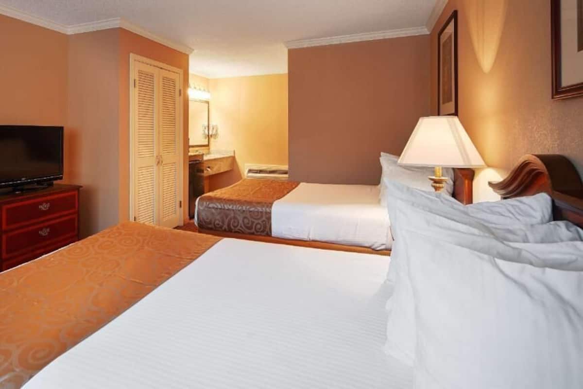 A hotel room with two beds, a TV, a desk, and a lamp.