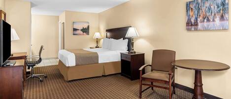 A hotel room with a bed, desk, chair, and table.