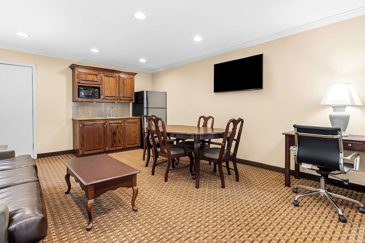 A room with a dining table, chairs, a sofa, a TV, a lamp, and kitchen appliances.