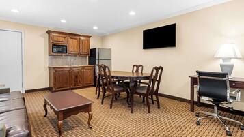 A room with a dining table, chairs, a sofa, a TV, a lamp, and kitchen appliances.