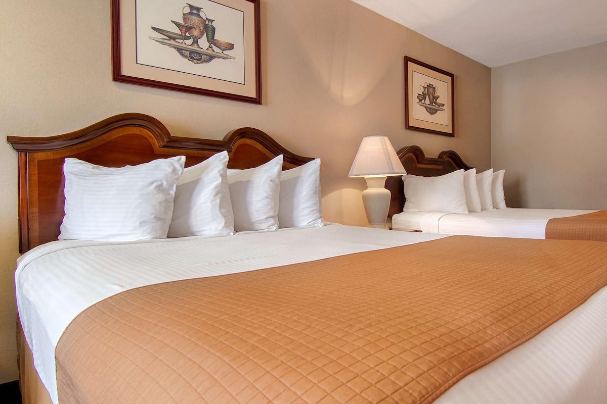 A hotel room with two beds, a nightstand, a lamp, and framed artwork on the wall.