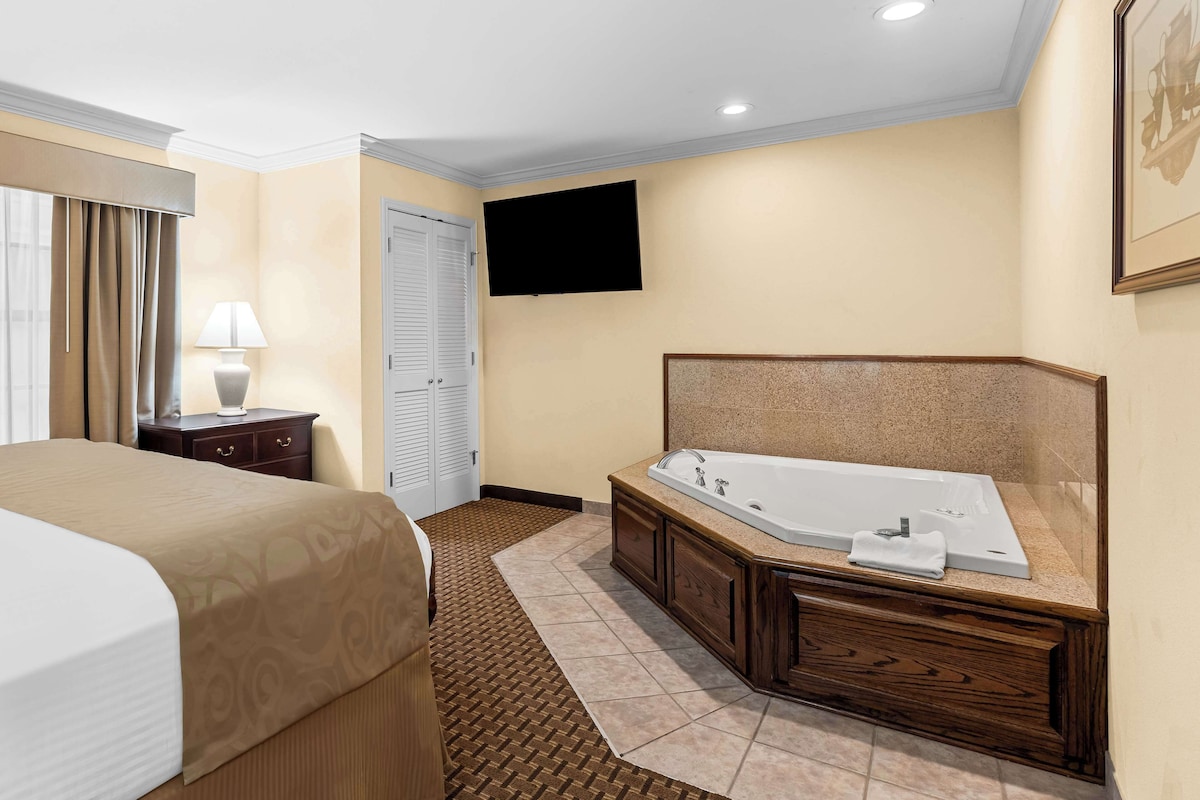 A hotel room with a large bed, a bathroom with a bathtub, a flat-screen TV, and a door.
