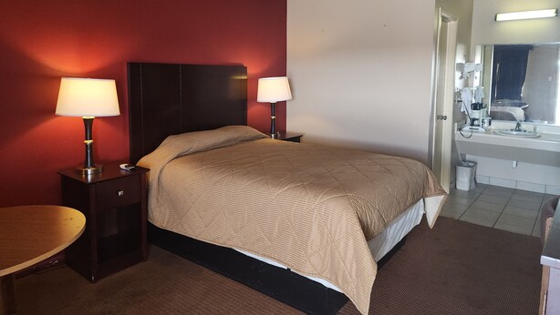 A hotel room with a bed, two bedside lamps, a small table, a bathroom with a sink and mirror, and a red accent wall. - Colonial Inn Monahans (Monahans)