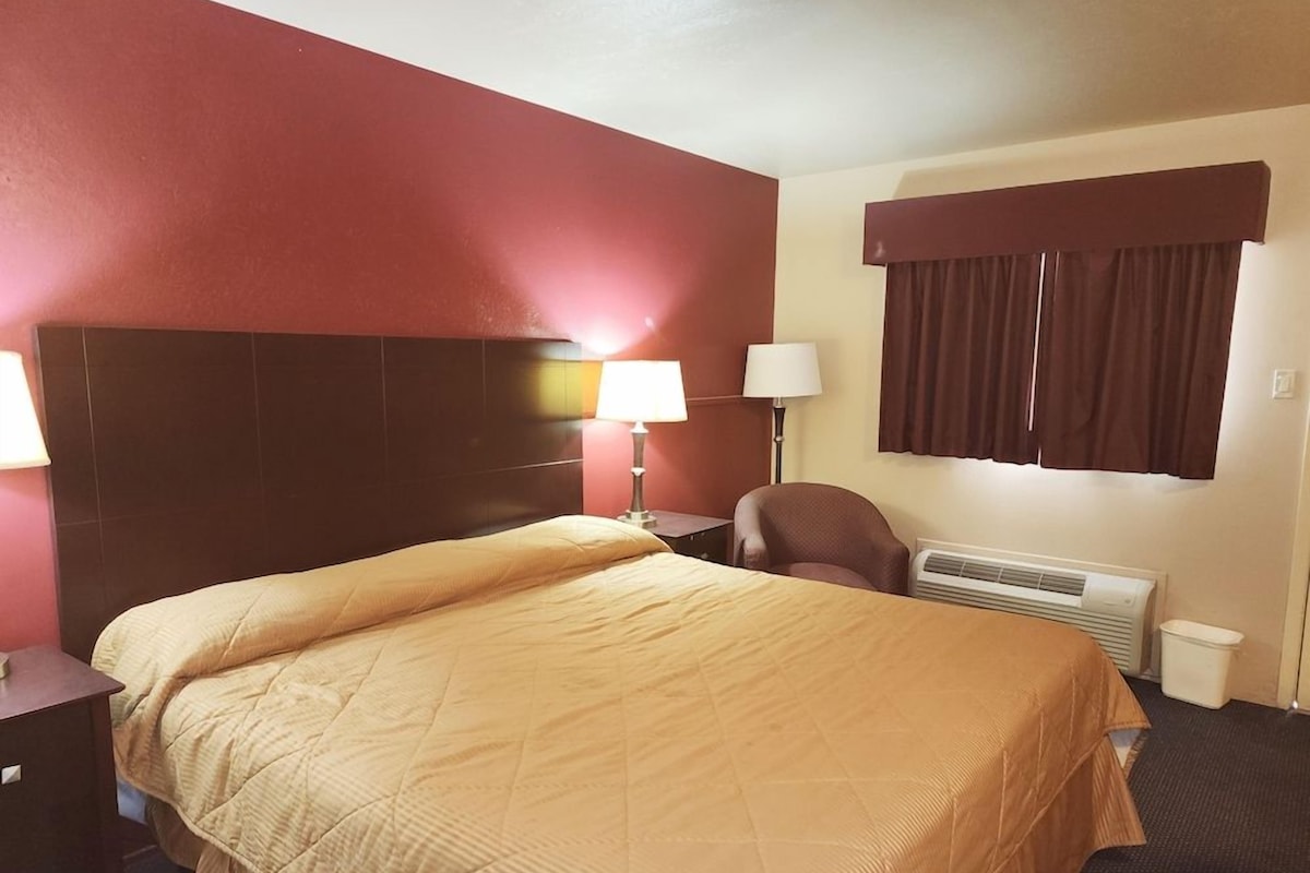 Ein Hotelzimmer mit einem großen Bett, einem Schreibtisch, einem Stuhl, einem Fenster mit Vorhängen und einem Wandheizkörper.