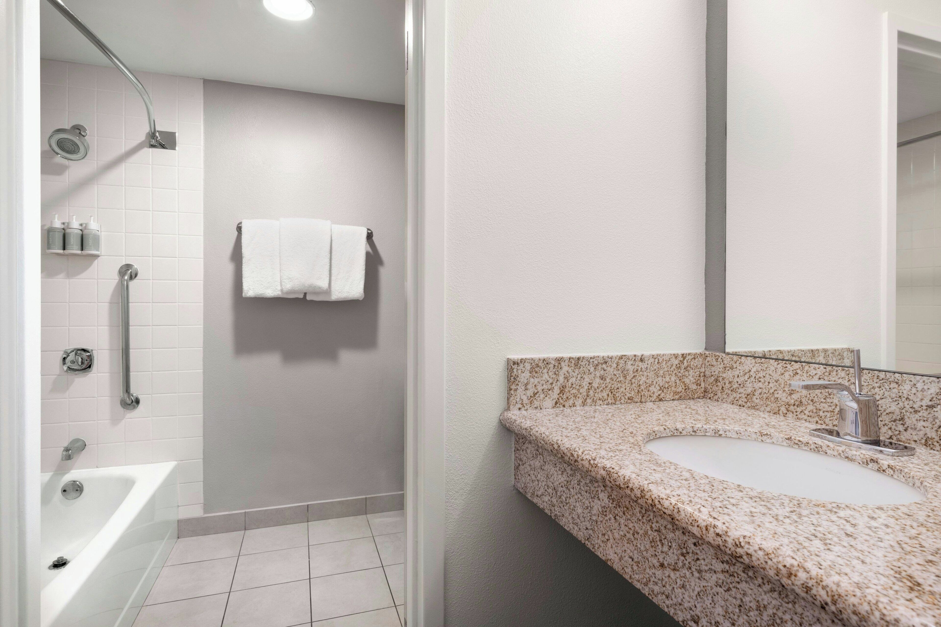 A bathroom with a white bathtub, a shower with a handheld showerhead, a granite countertop sink, and a wall-mounted towel rack.