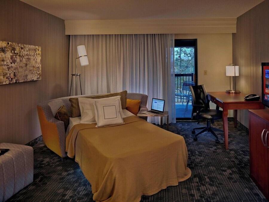 A hotel room with a bed, a desk with a laptop, a television, and a chair.