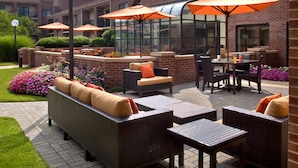Un patio al aire libre con mobiliario de mimbre, sombrillas naranjas y un edificio de ladrillo al fondo.