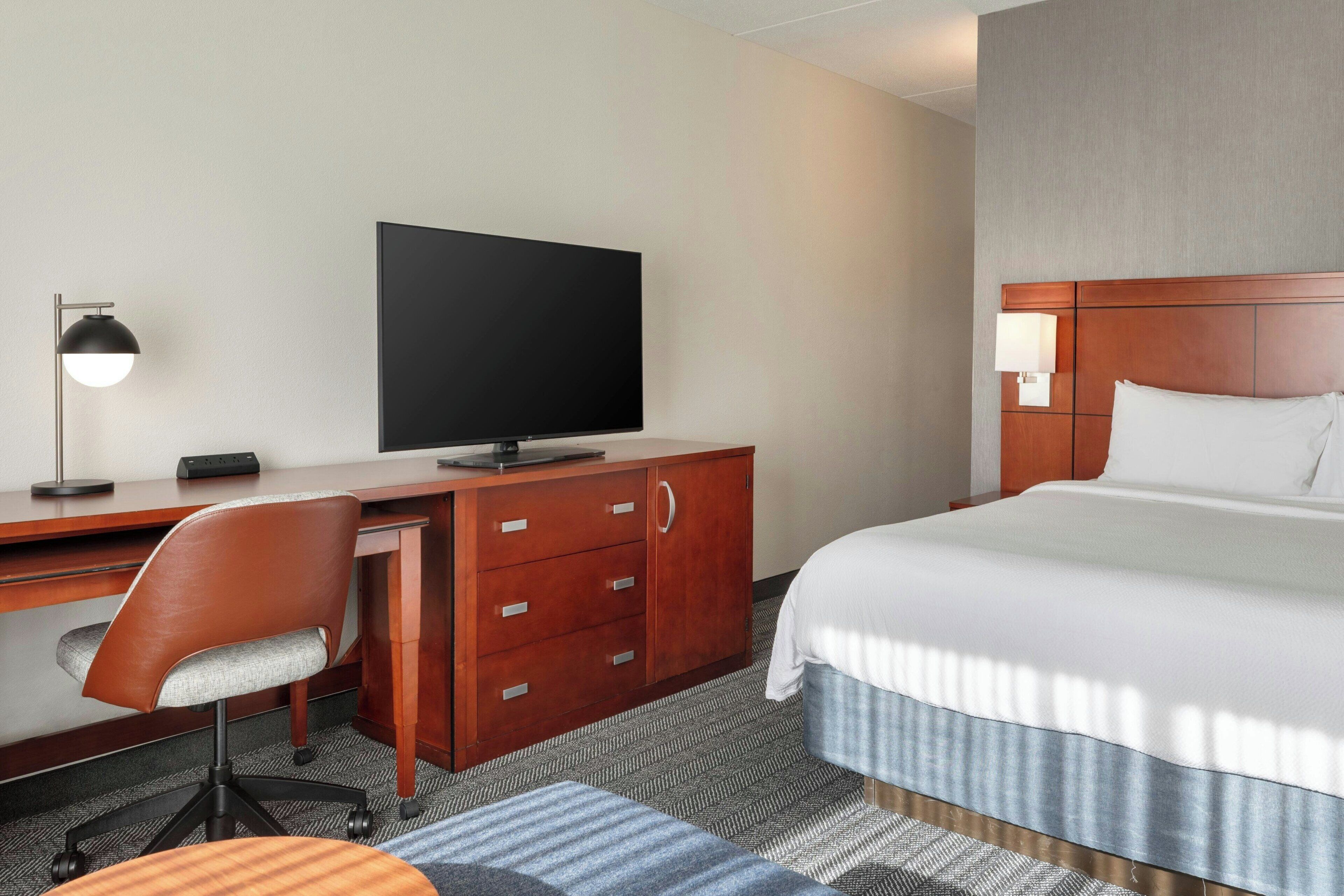 A hotel room with a bed, desk, chair, television, and a lamp.