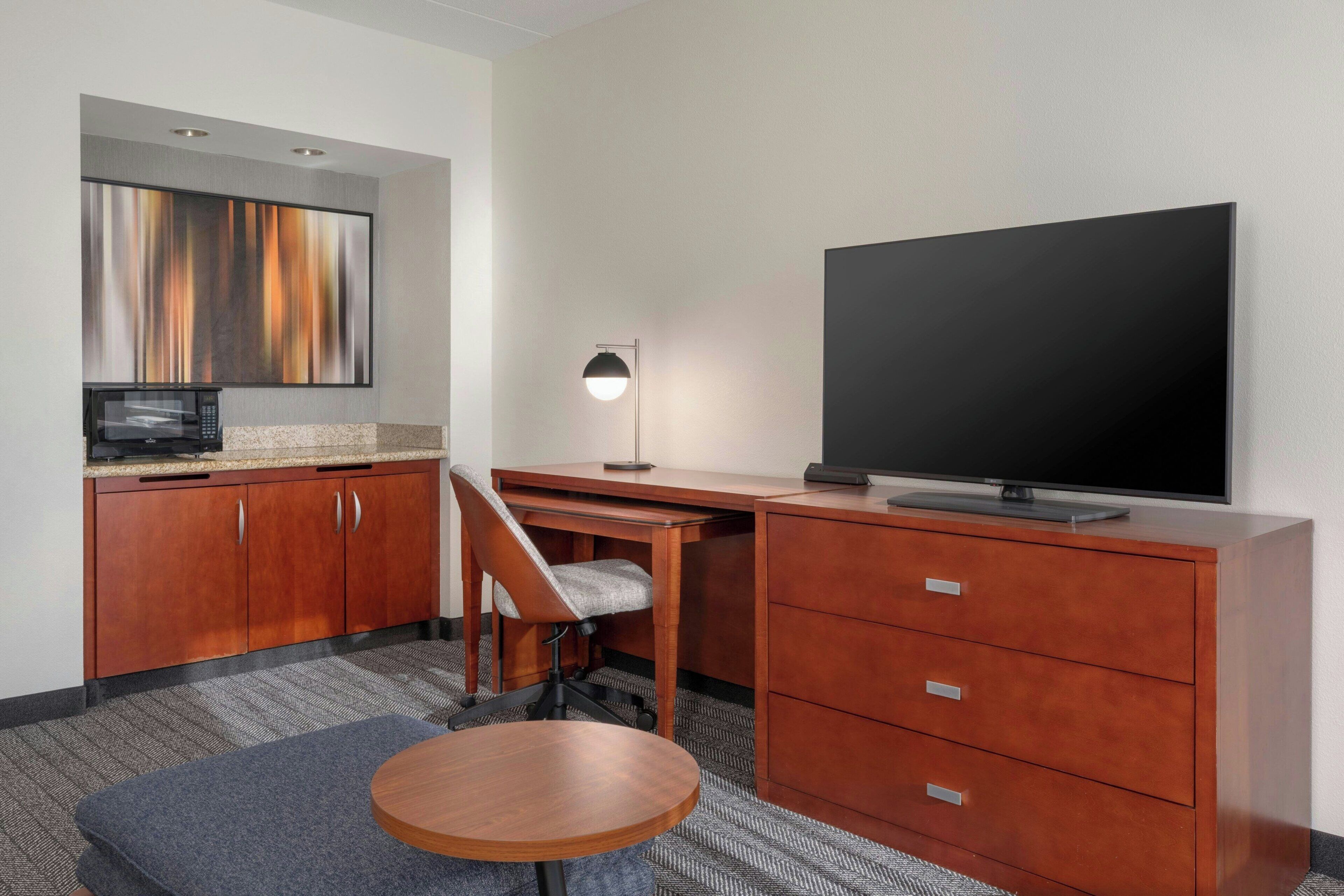 Una habitación de hotel con un escritorio de madera, una silla, un televisor, un microondas y un cuadro en la pared.