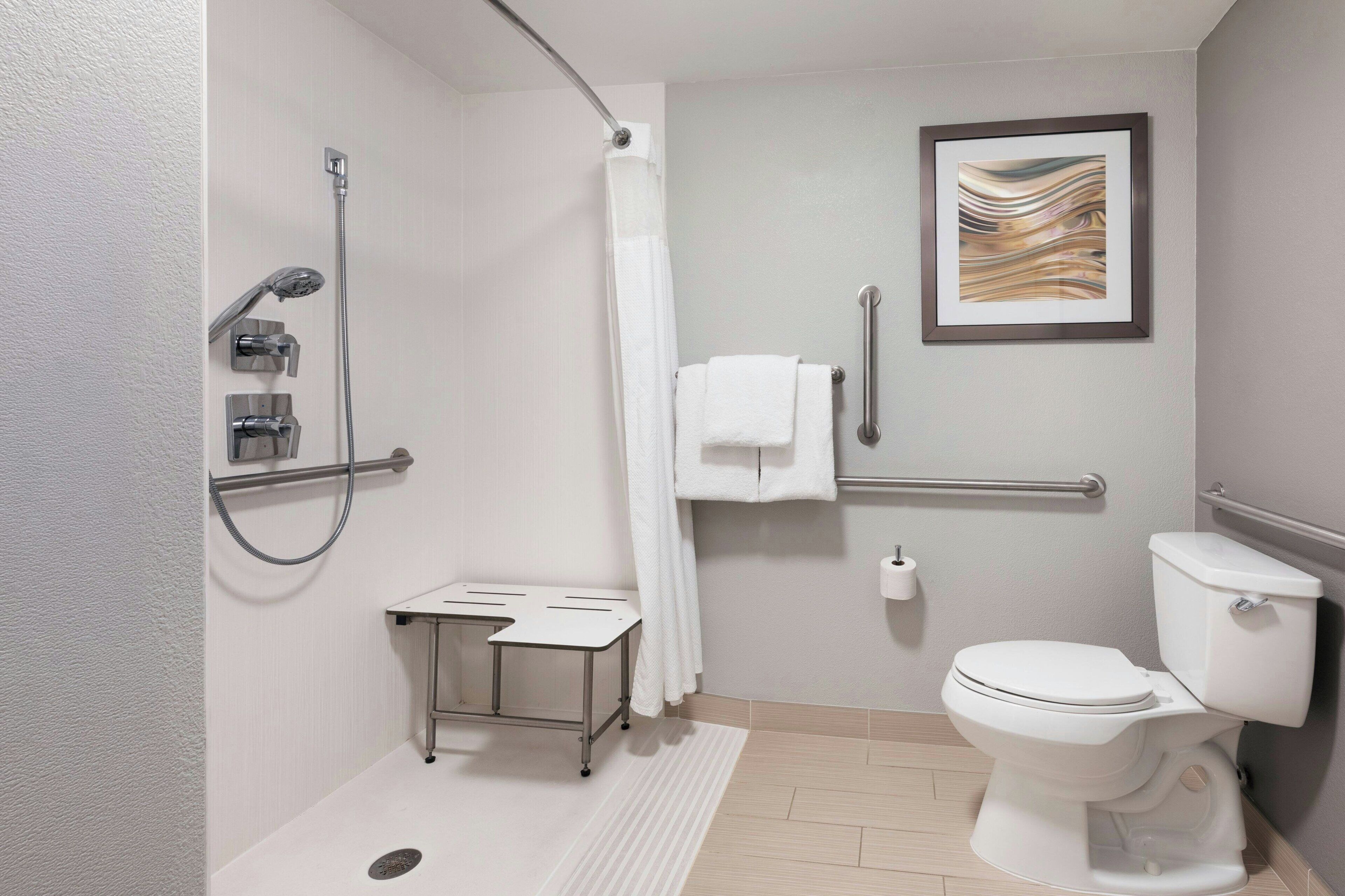 Un baño moderno con ducha, inodoro y una pequeña mesa con una toalla.
