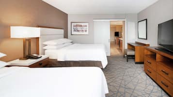 A hotel room with two beds, a desk, a TV, and a bathroom visible through an open door.