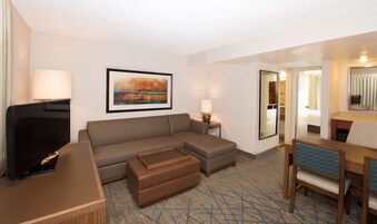 Habitación de hotel con sofá, reposapiés, televisor y escritorio con silla.