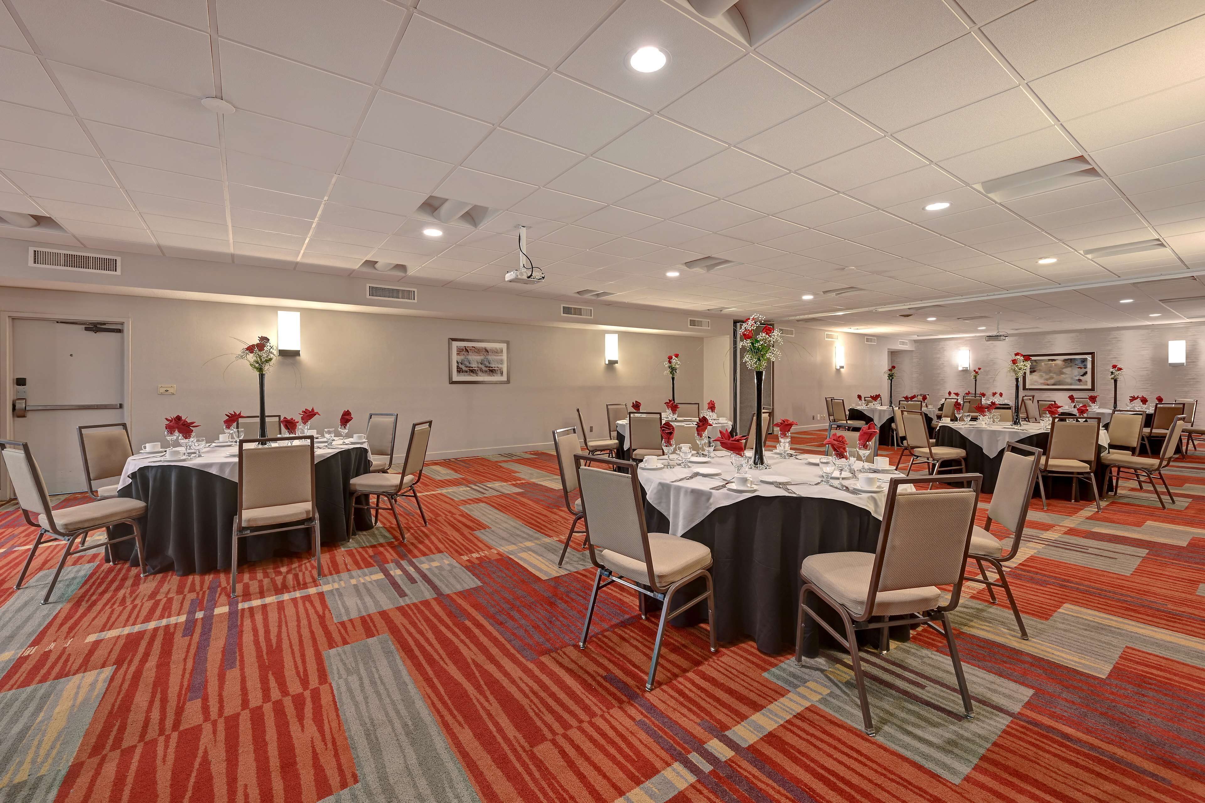Un salón de conferencias con mesas redondas, sillas y centros de mesa con flores.