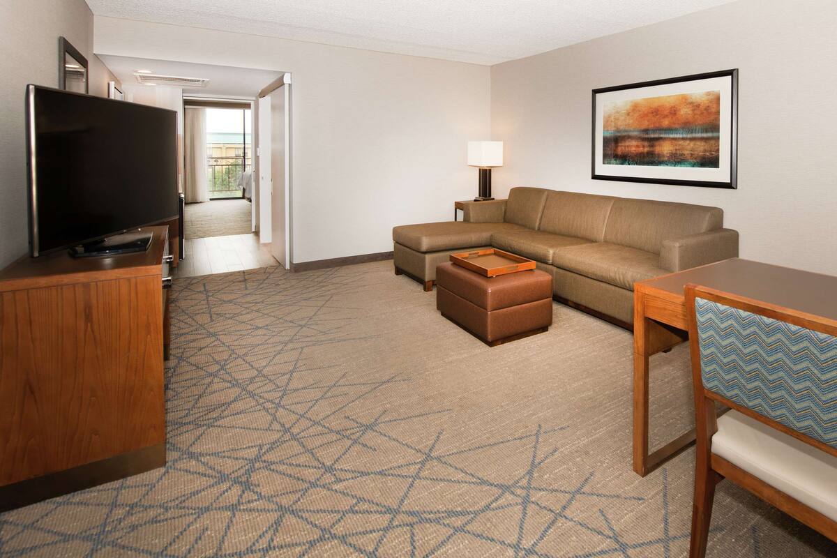 A hotel room with a flat-screen TV, a sofa, a dining table, and a chair.