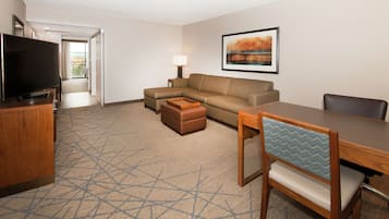 Una habitación de hotel con televisión de pantalla plana, un sofá, una mesa de comedor y una silla.
